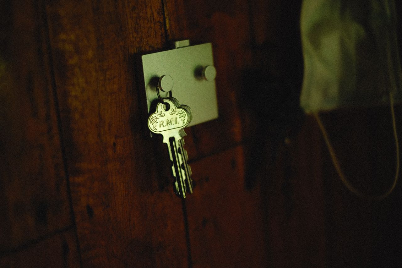 A close-up of a metallic key labeled R.M.I. on a rustic wooden wall hook.